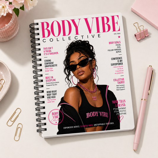 A spiral-bound notebook titled "BODY VIBE COLLECTIVE" lies open on a white surface, styled with a pink pen, binder clips, paper clips, and flowers around it. The cover features a magazine-style illustration of a woman in sunglasses and a black top with pink text. Notebooks, clothing, and accessories for body contouring specialists and beauty professionals.