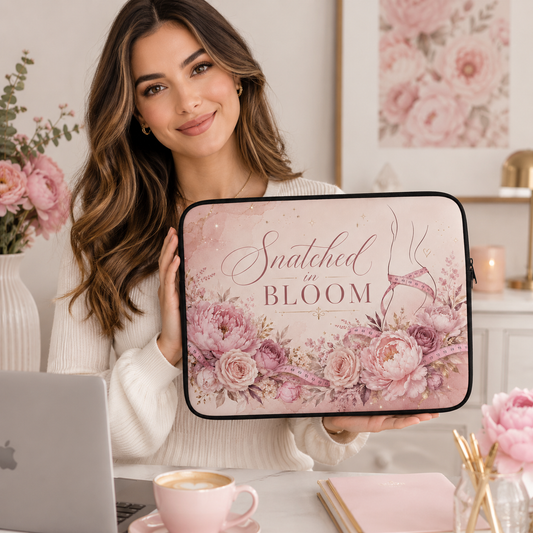 A woman holds a laptop sleeve featuring a pink floral design and the text 'Snatched in BLOOM'. The scene is set in a bright, cozy room with a laptop, coffee cup, and framed floral art in the background. Laptop sleeves, notebooks, clothing, and apparel for body contouring specialists and beauty professionals.