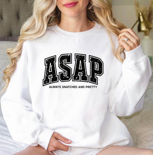 A woman wearing a white crewneck sweatshirt with 'ASAP' and 'ALWAYS SNATCHED AND PRETTY' printed in black varsity-style lettering on the front. Clothing, apparel and accessories for body contouring specialists and beauty professionals.