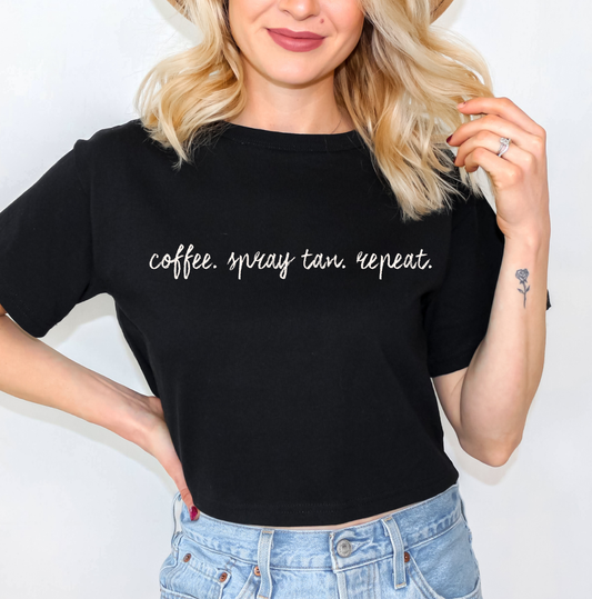 A woman wearing a black short-sleeve graphic t-shirt with the text 'it's giving dehydrated' printed in white lowercase letters, paired with light blue jeans against a plain white background. Graphic t-shirts and apparel for spray tan artists, and beauty professionals.