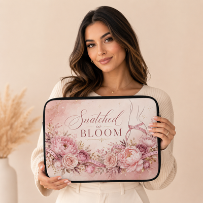 A woman holds a laptop sleeve featuring a pink floral design and the text 'Snatched in BLOOM'. The sleeve has a black border and is shown against a warm beige background. Laptop sleeves, notebooks, clothing, and apparel for body contouring specialists and beauty professionals.