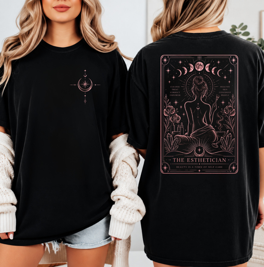 Two women modeling a black oversized T-shirt, showing both the front and back. The front has a small rose gold celestial compass graphic on the left chest. Clothing, apparel and accessories for estheticians, and beauty industry professionals.
